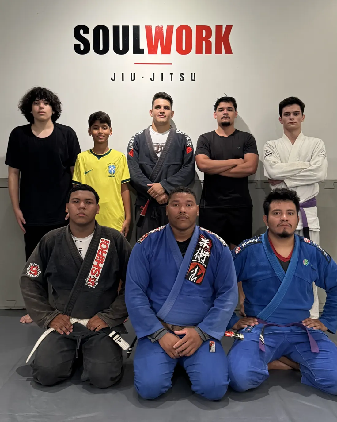 Turma adulta da Soul Work em frente ao logo da equipe, com o professor Gabriel no centro