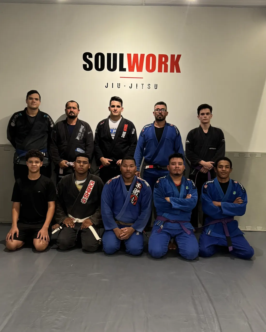 Alunos da turma adulta da Soul Work de kimono, ajoelhados e em pé na frente do logo